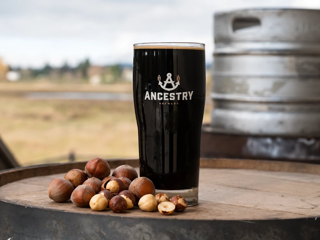 A pint of Hazelnut Stout with hazelnuts on a barrel